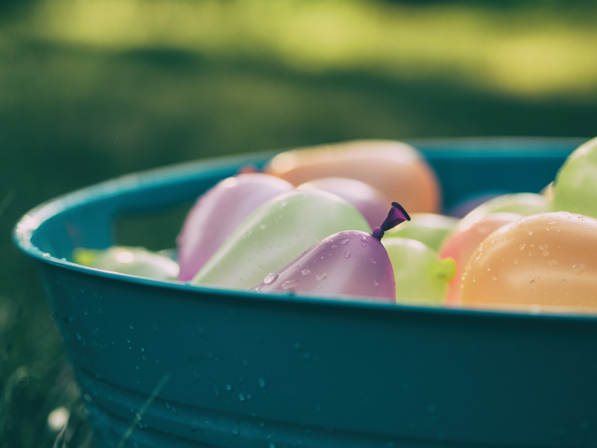 A bucket of pastel colored water balloons outside on a sunny summer day.  What happens next?