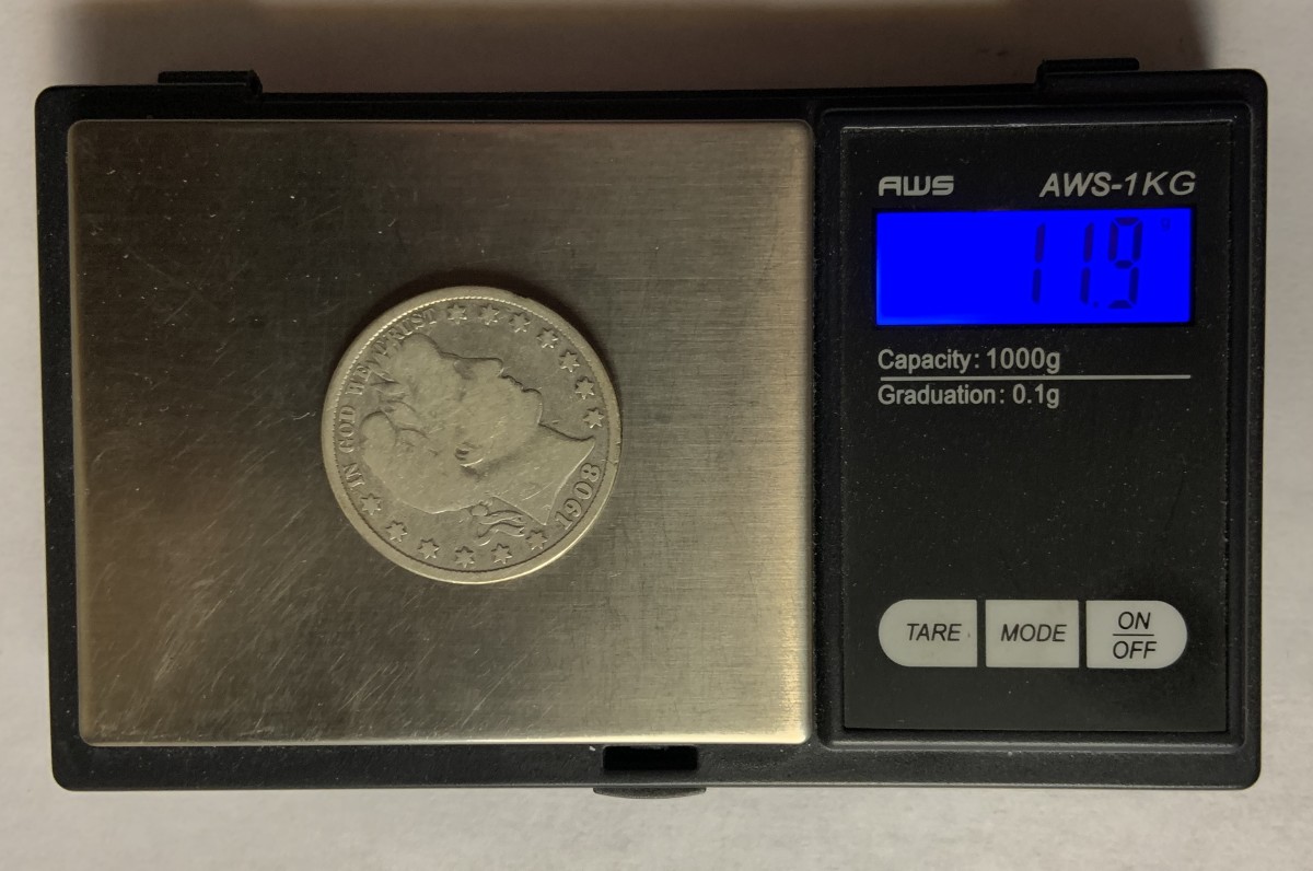 Electronic scales measuring weight of a coin. The coin shown is a genuine and has a mint specified weight of 12.5 grams. The wear on the coin has reduced the weight to 11.9 grams.