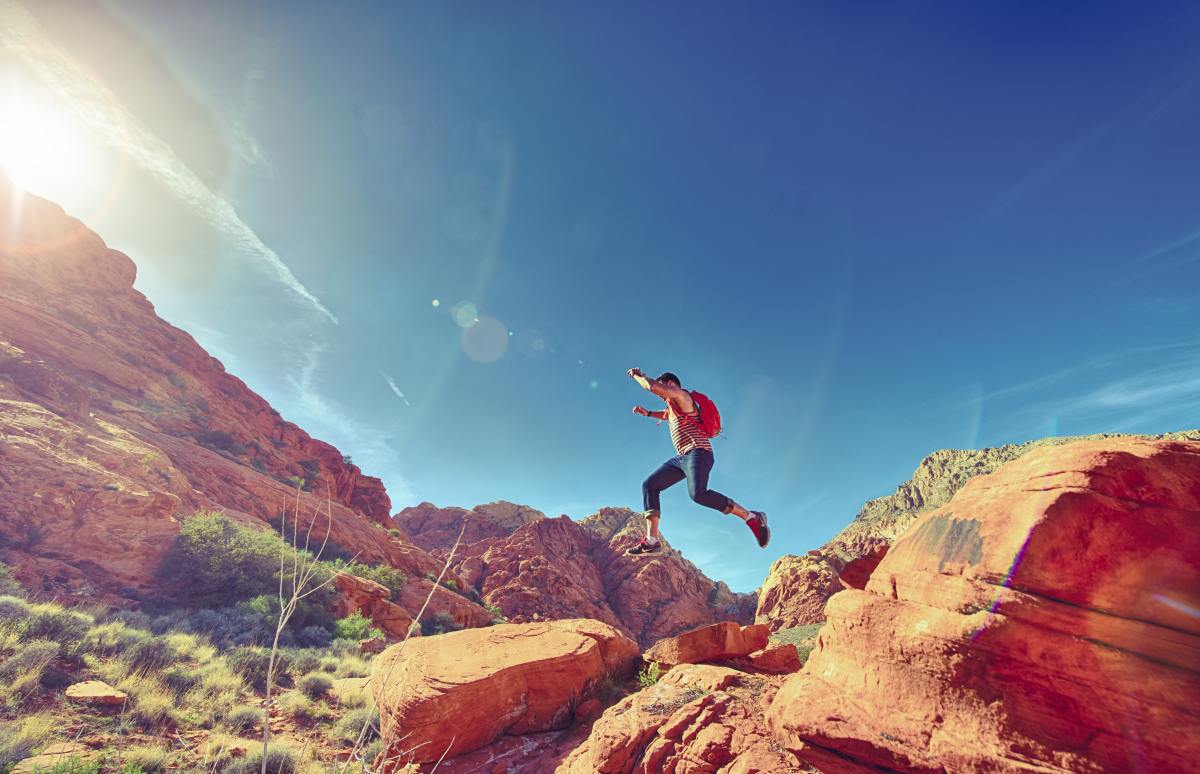 Hiker leaps over rock formations in the desert.