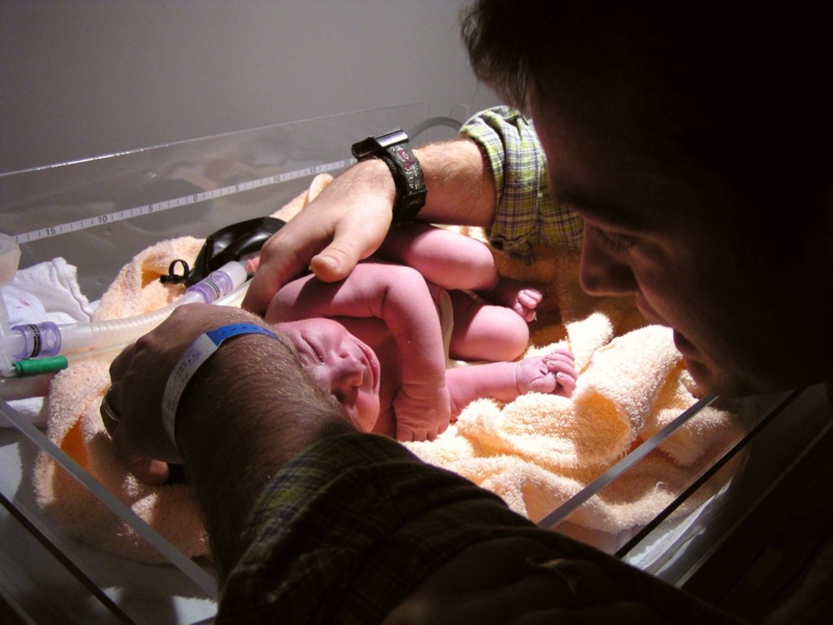 Father gives attention to his newborn daughter in a hospital warming tray. 