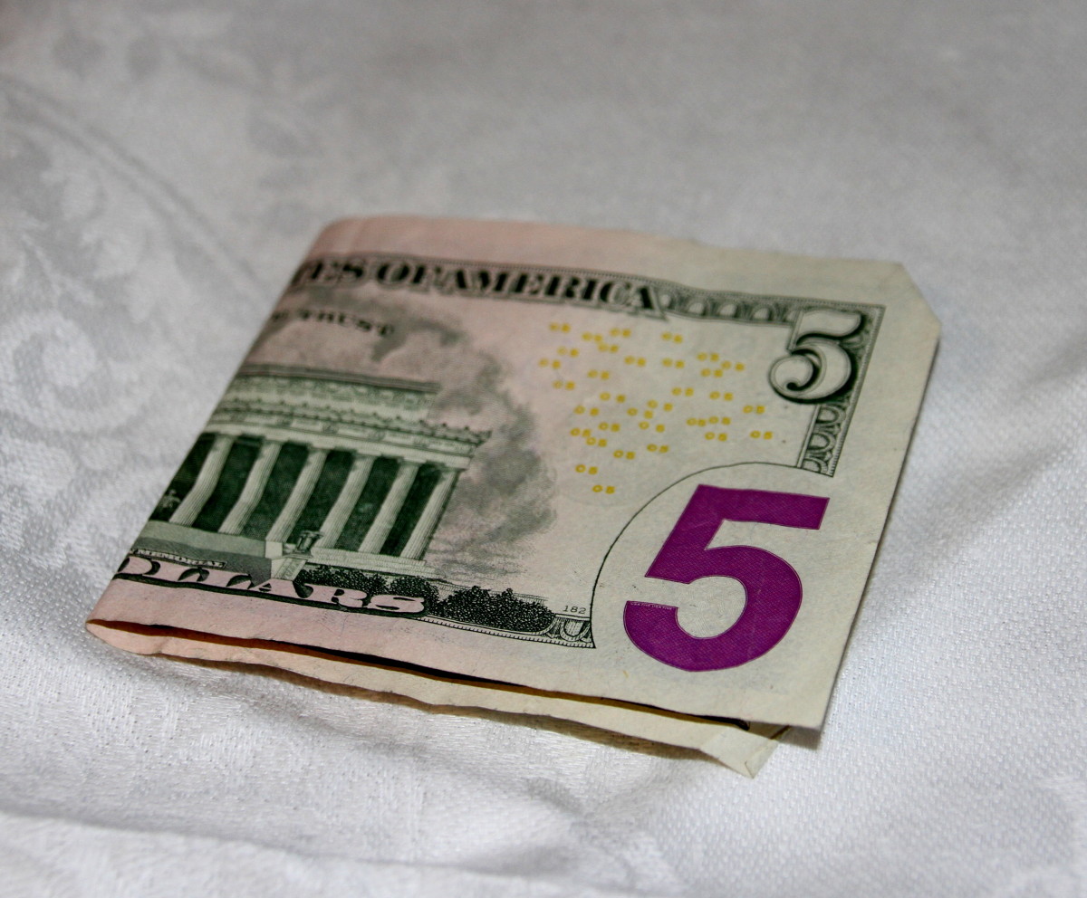 Five dollar bills are folded with short sides together.