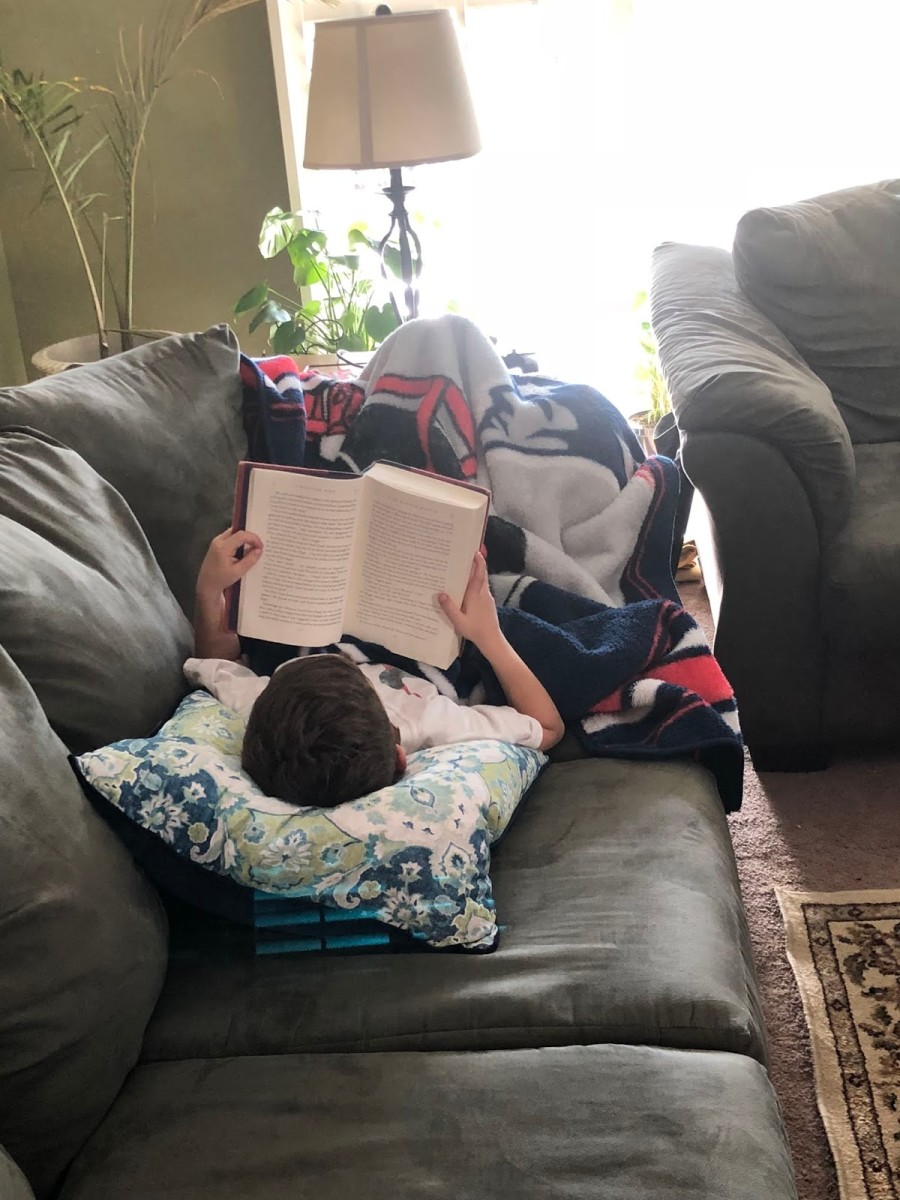 My son reading Harry Potter on the couch.