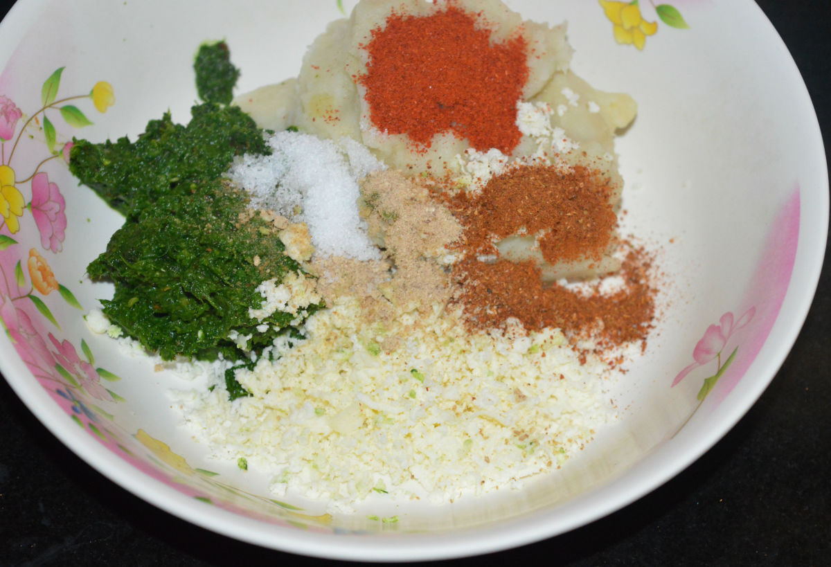 Step four: Add the leafy greens paste, grated paneer, mashed potatoes, red chili powder, spice powder or garam masala powder, raw mango powder, and salt. Mix well to prepare a firm dough. 