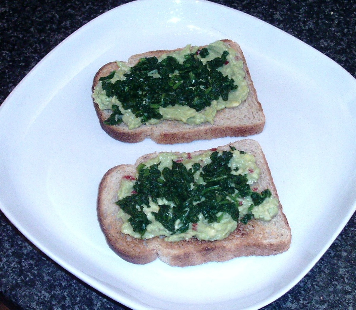 Spinach is scattered over guacamole on toast
