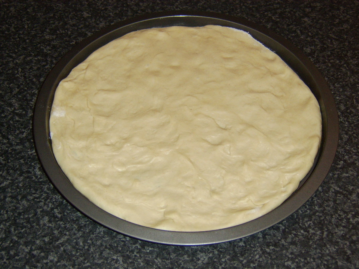 Pizza dough is stretched out in baking tin