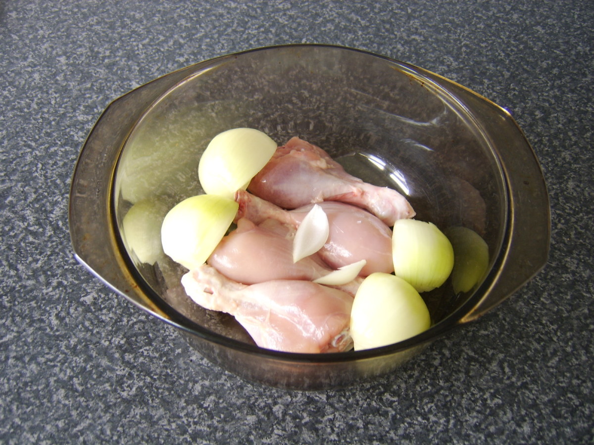 The chicken drumsticks are skinned and laid in the base of a large casserole dish with the quartered onion