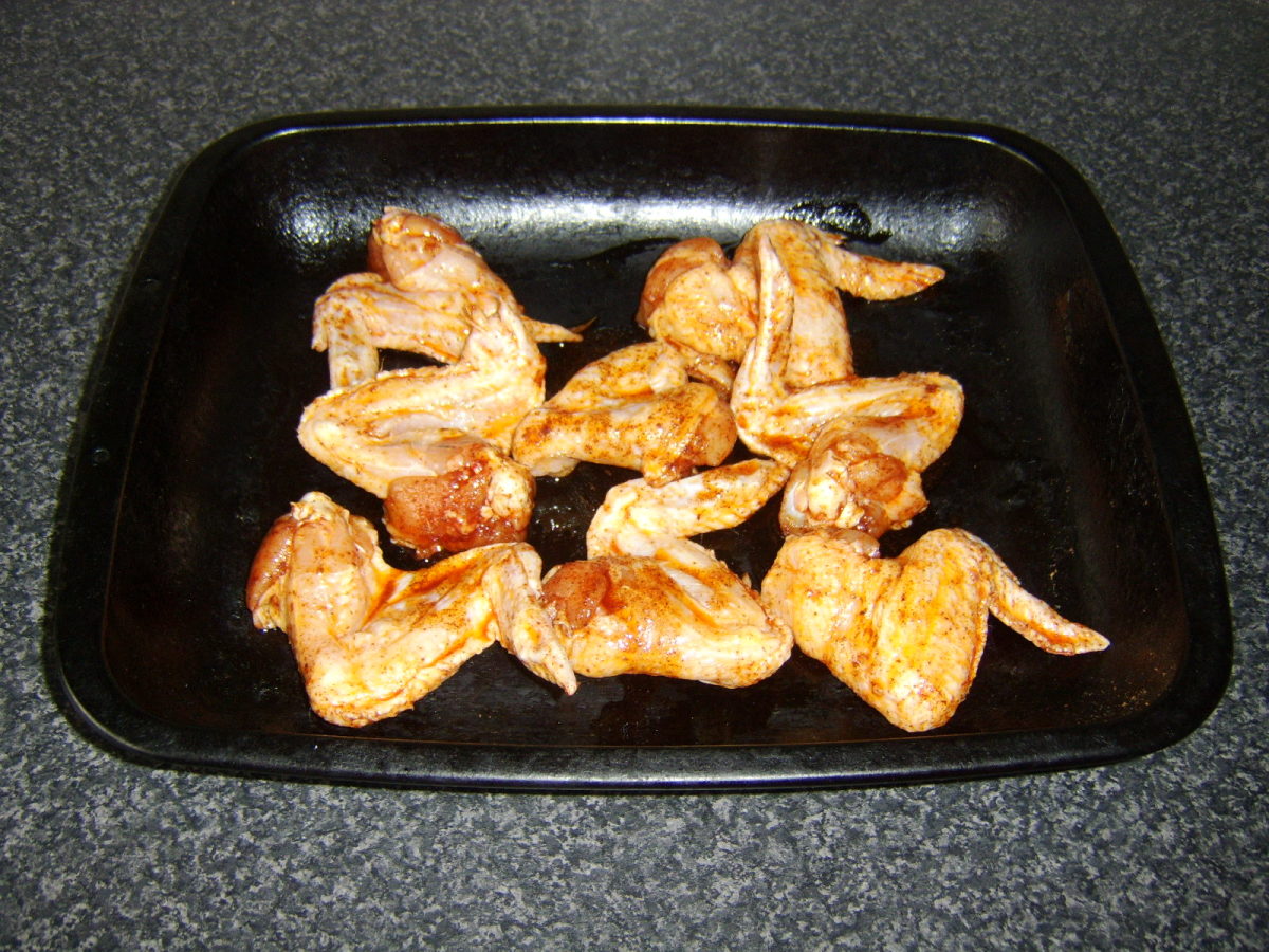 Marinated chicken wings are laid in a single layer on a large roasting or baking tray