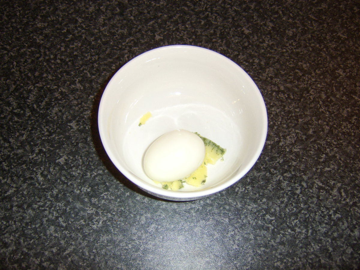 Hard boiled egg is mashed in a bowl with herb butter.