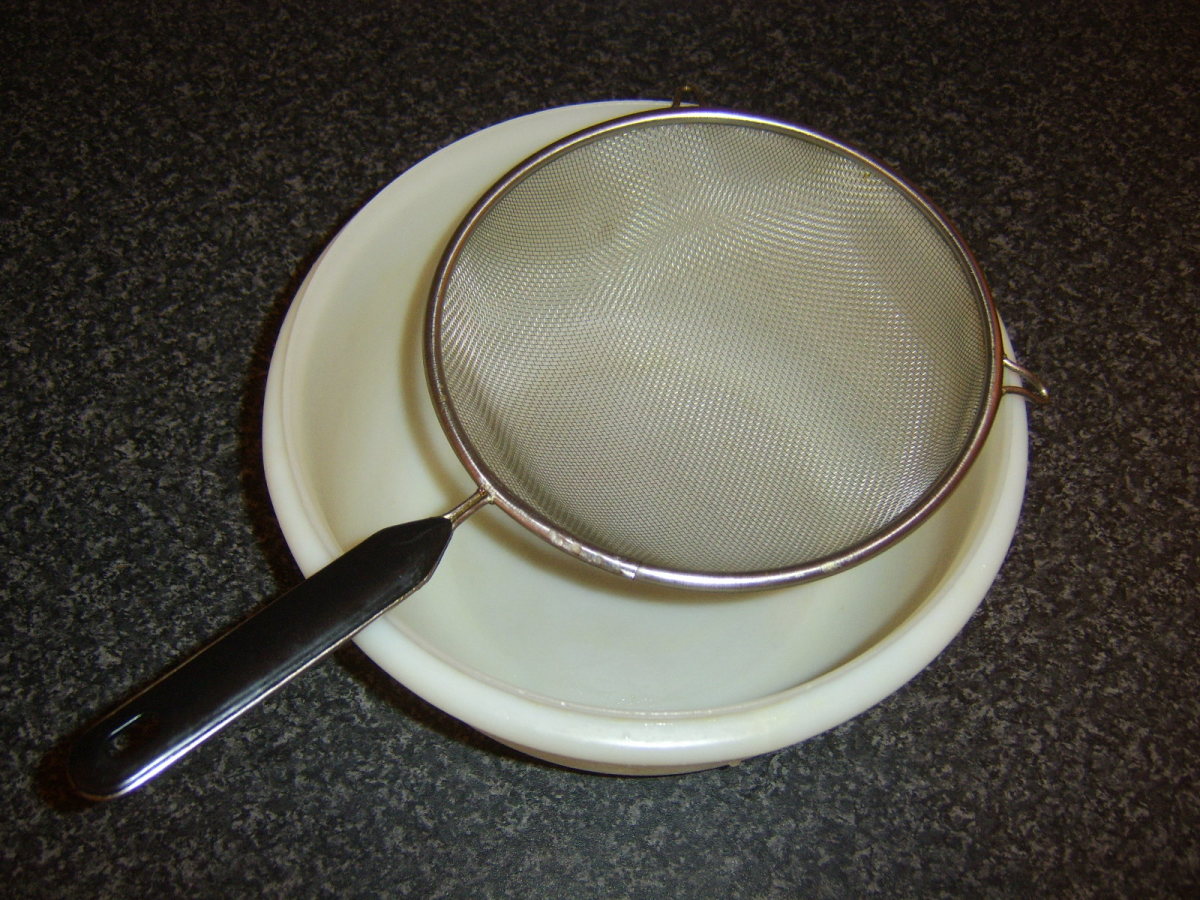 A fine sieve is suspended over a large bowl to strain the lamb stock.