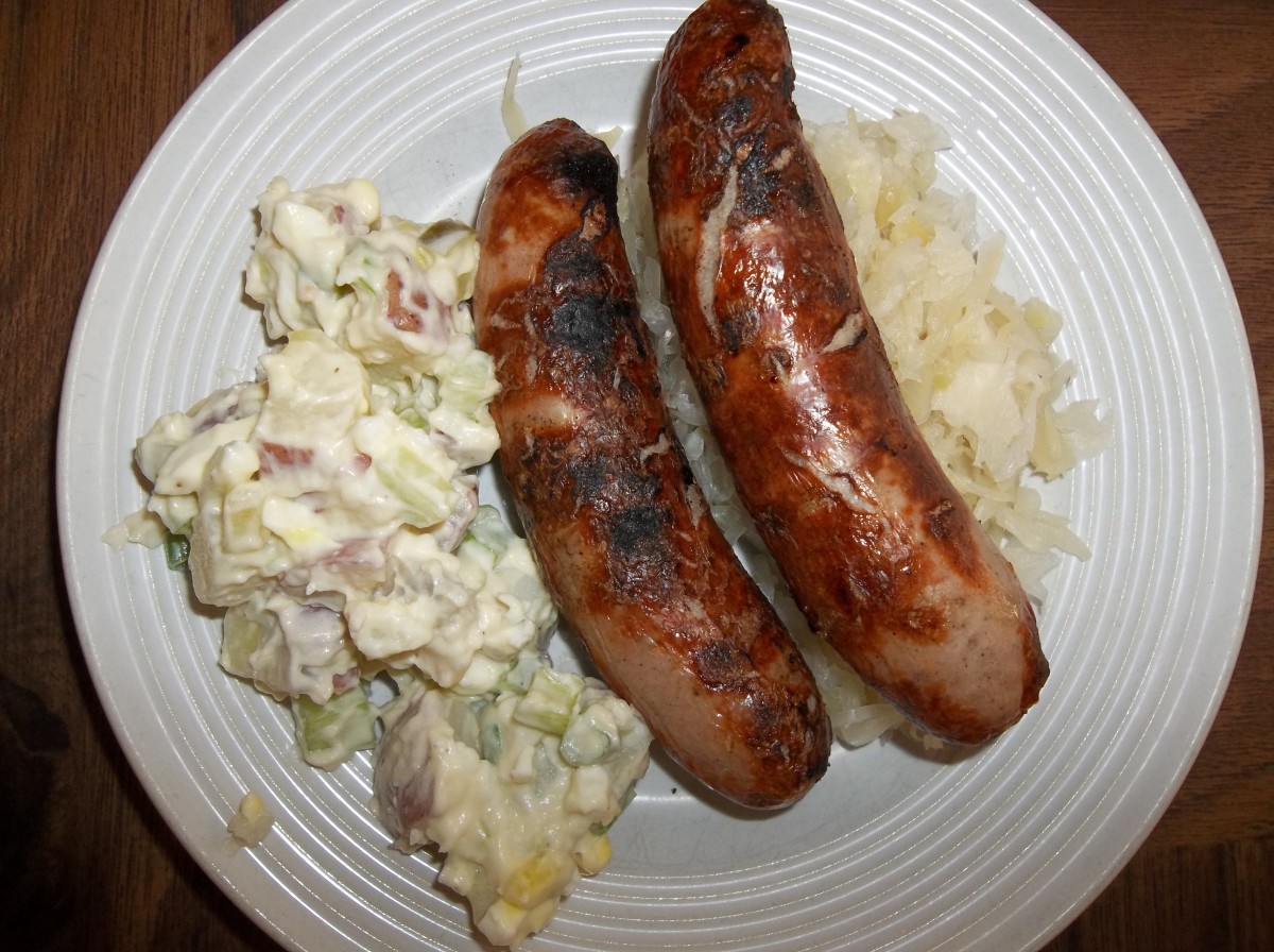 Potato salad with a bed of of sauerkraut holding up a couple of Bratwursts.