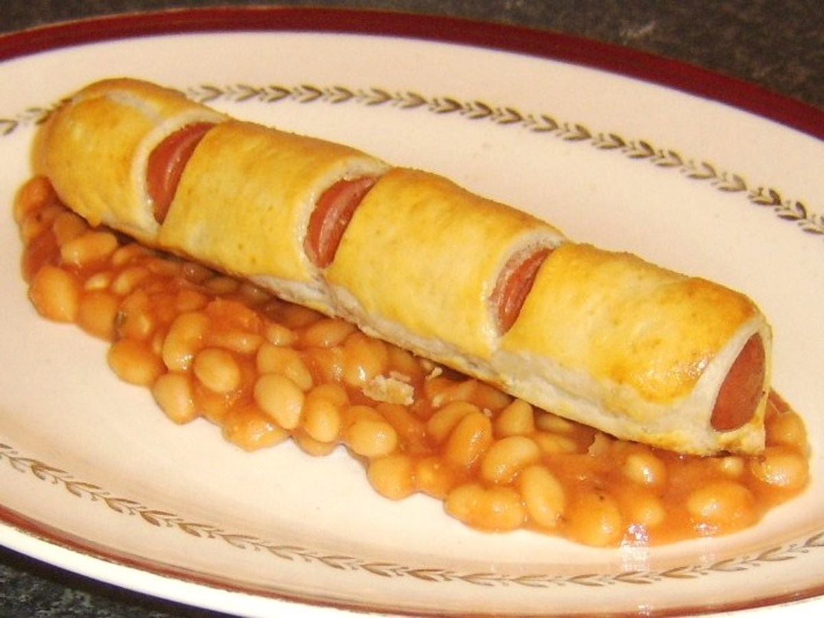 Hot dog wrapped and cooked in puff pastry on a bed of baked beans in tomato sauce