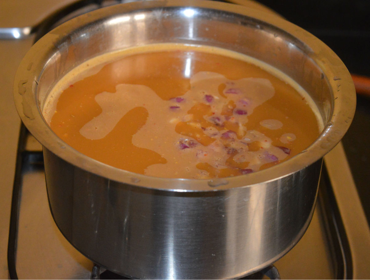 Step five: Take horse gram water in a sauce pan. Add spice paste, turmeric powder, jaggery, chopped onions, salt, and some hing. Add water as per instructions.