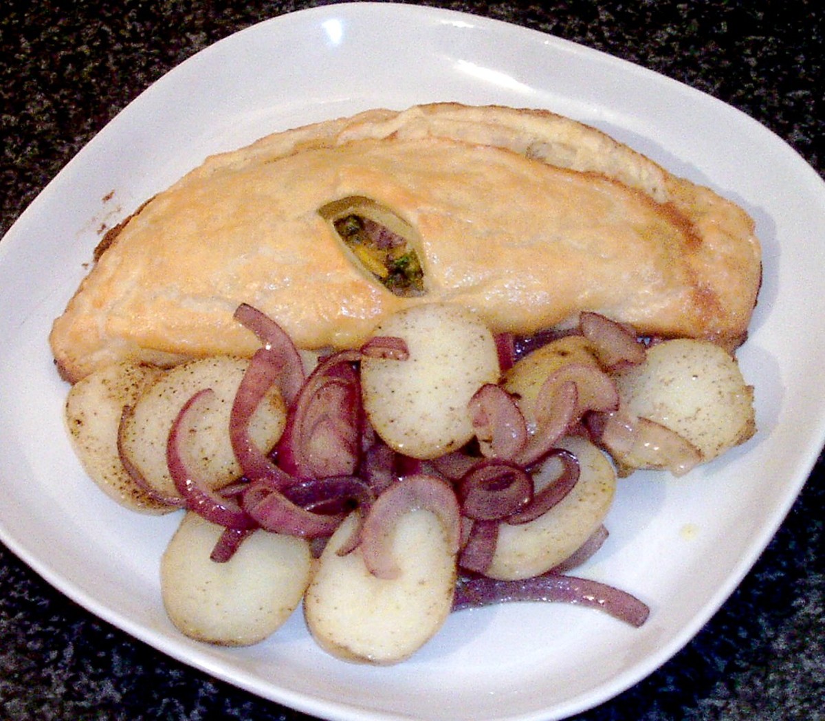 Sea bass en croute and sauteed potato and onions are plated.
