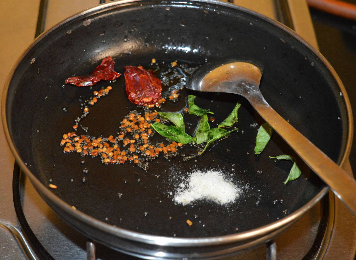 Step three: Heat oil in a deep-bottomed pan.  Keep the heat low. Throw in fenugreek seeds. Saute them until they emit a nice flavor or they turn golden brown. Throw in broken dry red chilies, curry leaves, and hing powder. Mix well. 