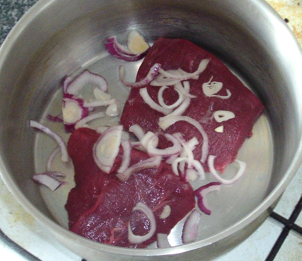 Venison haunch in pot with sliced onion