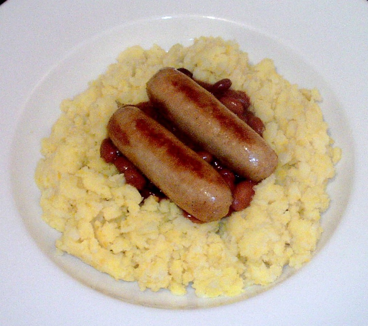 Chicken sausages are served on a bad of turmeric mash and a well of mixed beans in spicy tomato sauce