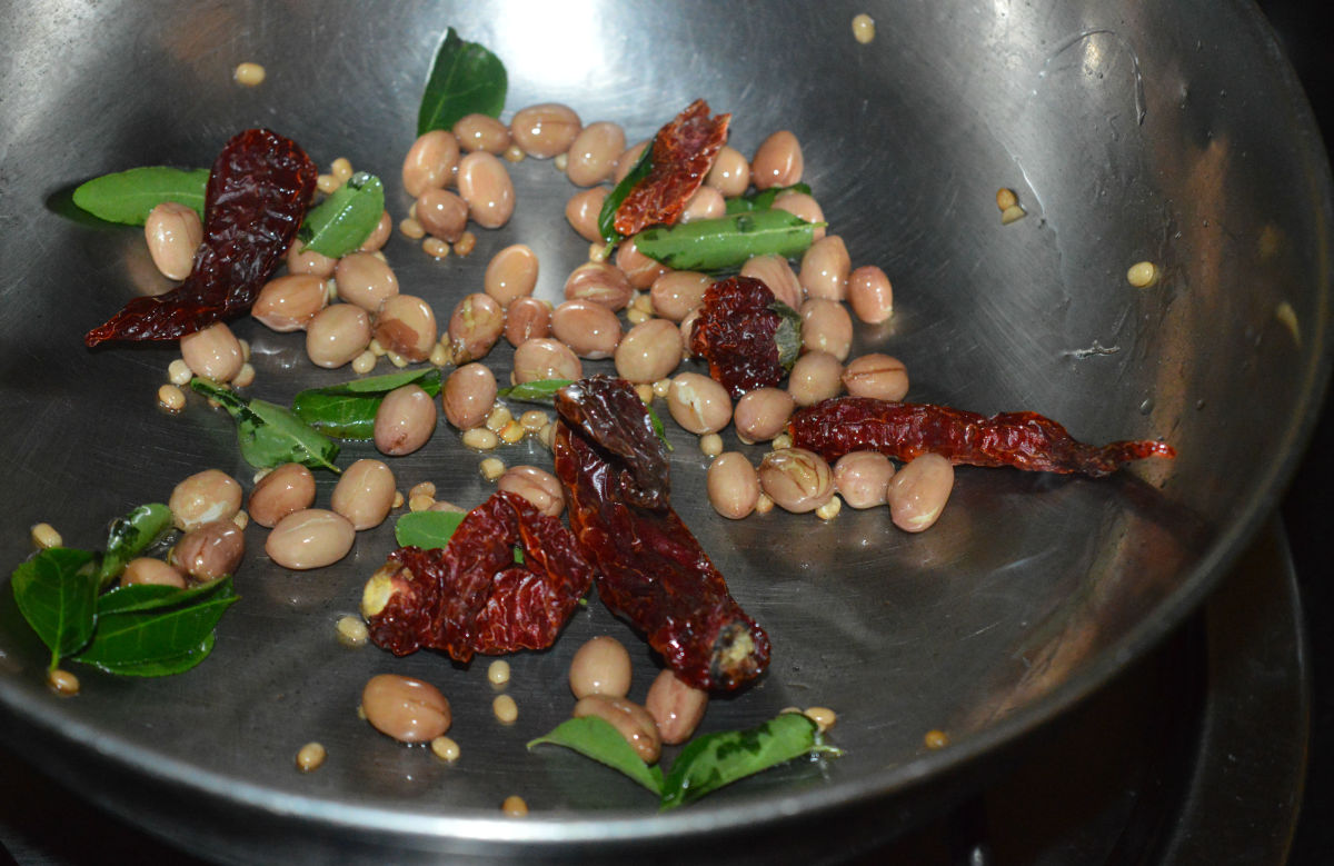 Step 2: Heat a teaspoon of oil in a pan. Add peanuts and white lentils. Saute until they become crispy. Throw in curry leaves and broken red chilies. Saute for 20 seconds. 