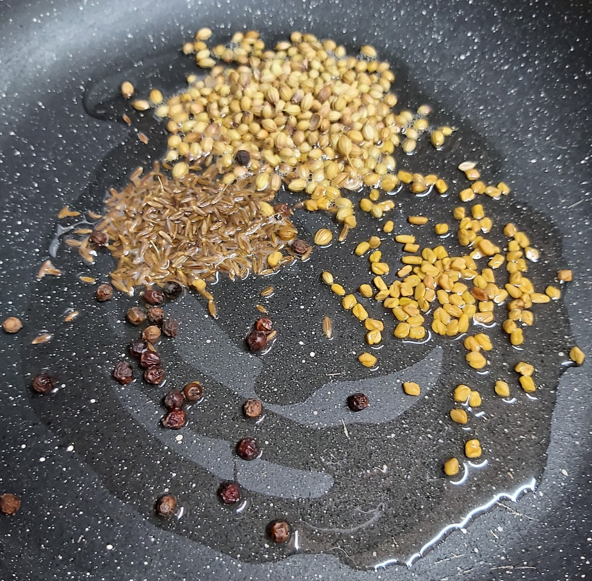 In a frying pan, heat 1 teaspoon of oil. Add 1 tablespoon of coriander seeds, 1 tablespoon of cumin seeds, 1/2 teaspoon fenugreek seeds, and 1/2 teaspoon of whole black peppercorns.
