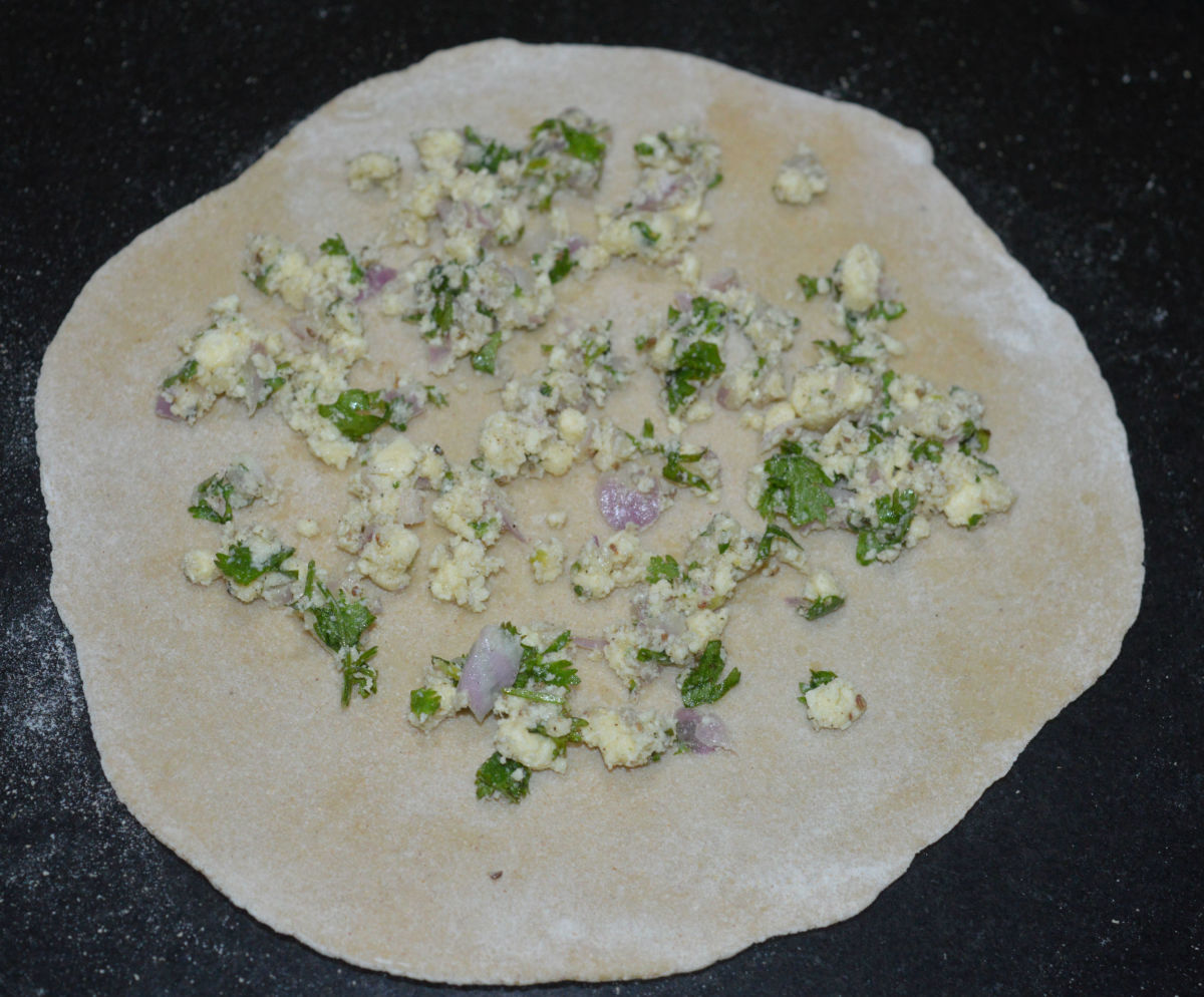 Step three: Pinch out a lemon-sized dough portion. Roll it to make a disc of 6-8 inches diameter. Spread about a tablespoon of the paneer stuffing on it.