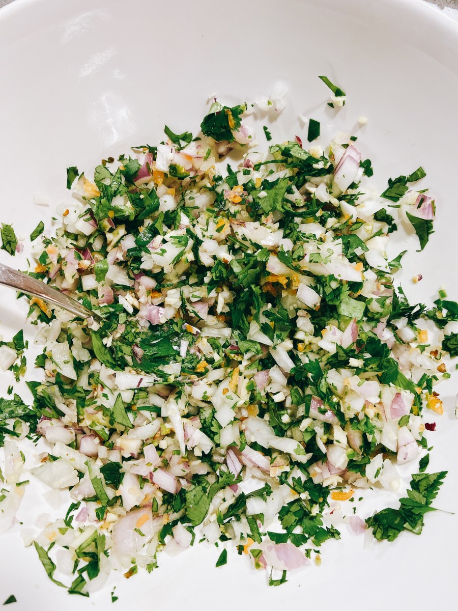 In a large bowl, combine the chopped garlic, onion, cilantro leaves, serrano, and habanero pepper. 