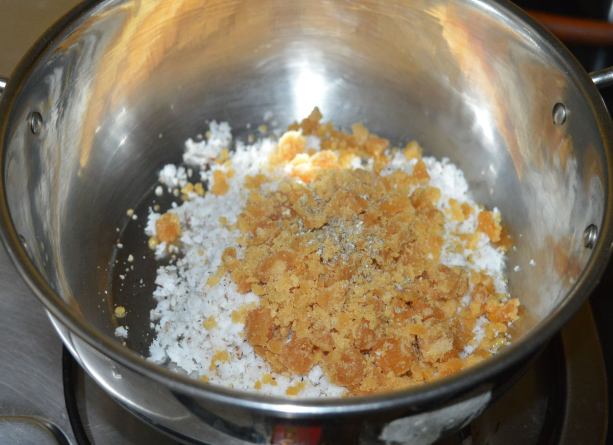 Step two: Heat a deep-bottomed pan containing jaggery powder, cardamom powder, and grated coconut. Add a few drops of water to loosen the mixture. 