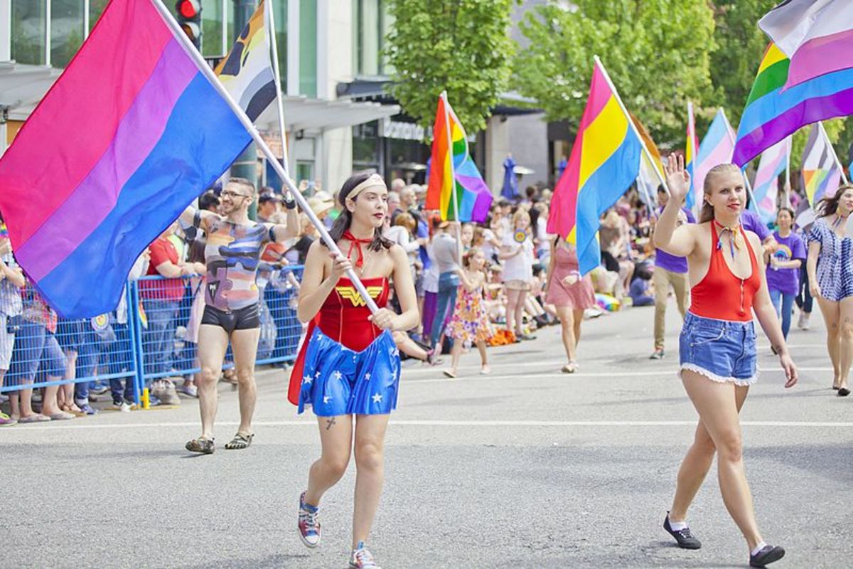 A bi women marching in a modern Pride parade, dressed as Wonder Woman.