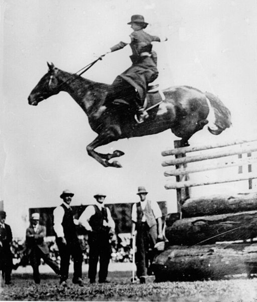A woman performing a 6'6" high jump over an obstacle while riding sidesaddle.