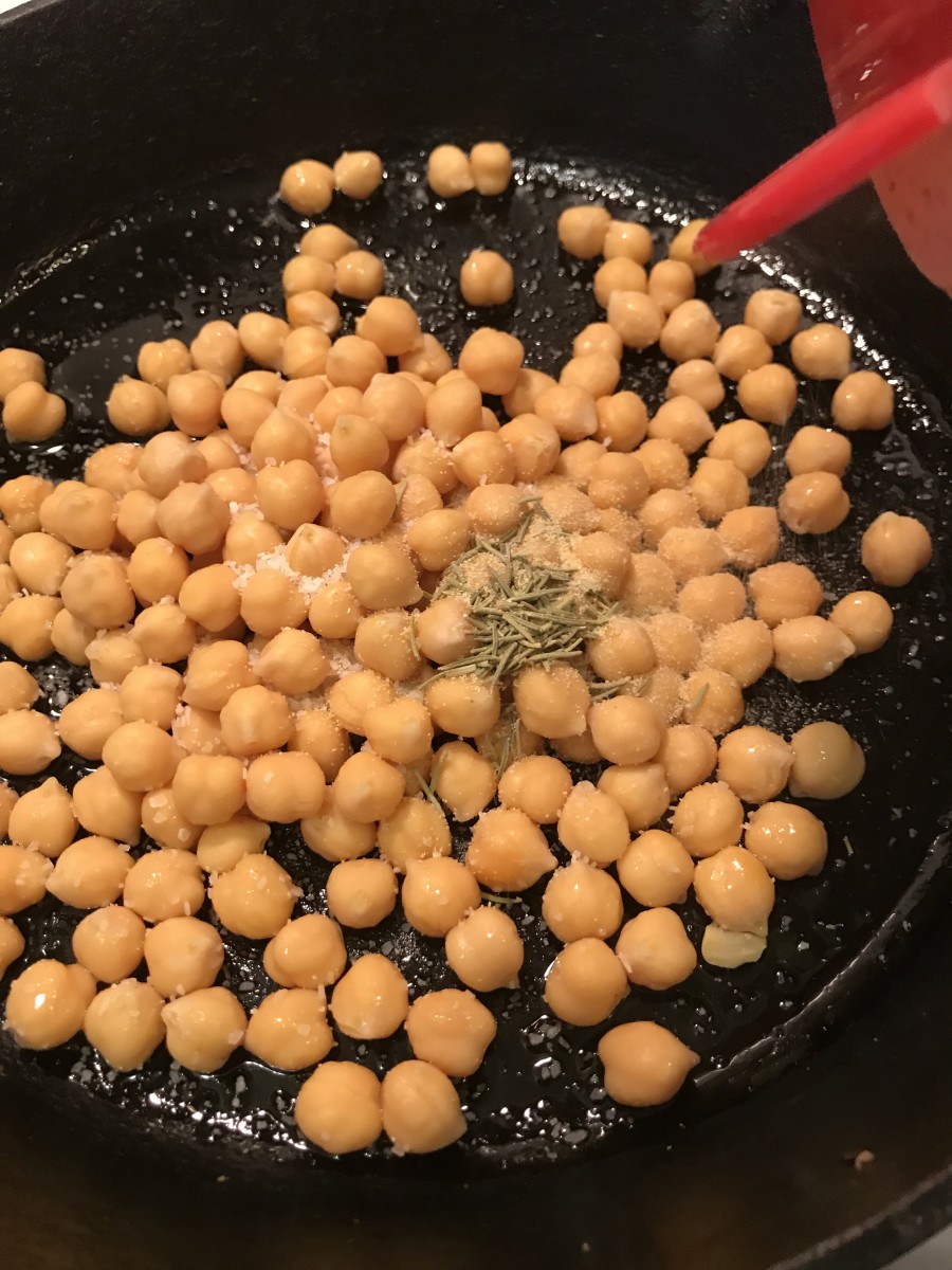 Go ahead and toss on the seasonings. They'll adhere to the chickpeas because of the oil, but they'll also toast themselves. The rosemary especially will become fragrant as it 'blooms' in the hot oil.