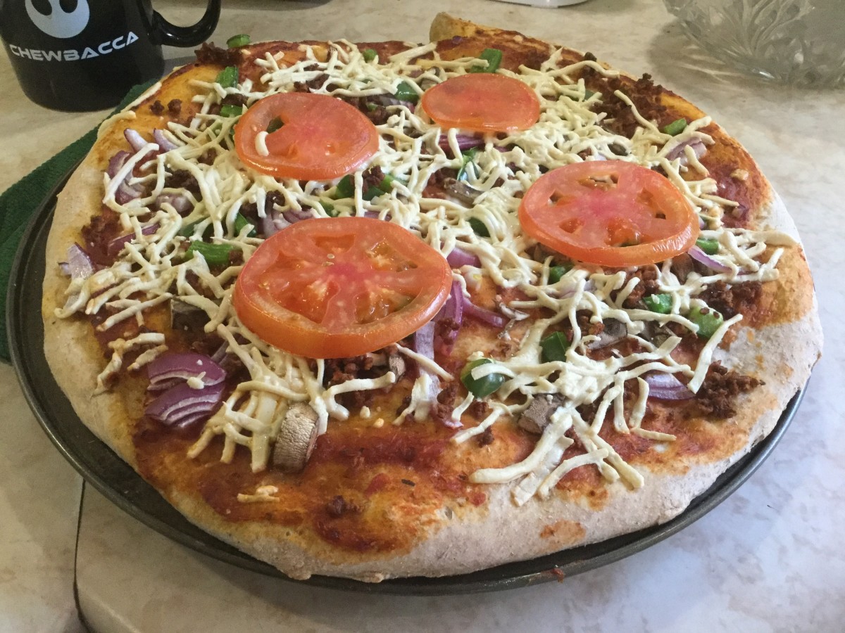 Homemade pizza dough topped with tomato sauce and slices, mushroom, red onion, green pepper, and vegan shredded cheese.