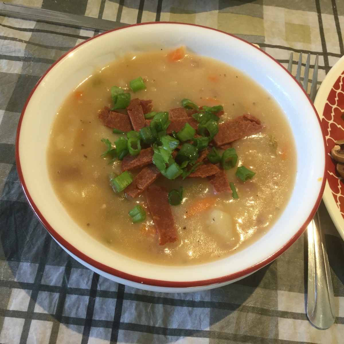 Vegan potato soup topped with green onion and sliced vegan bacon.