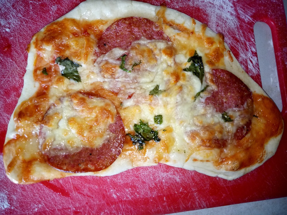 Individual size home made pizza with toppings of salami, cheese and basil.