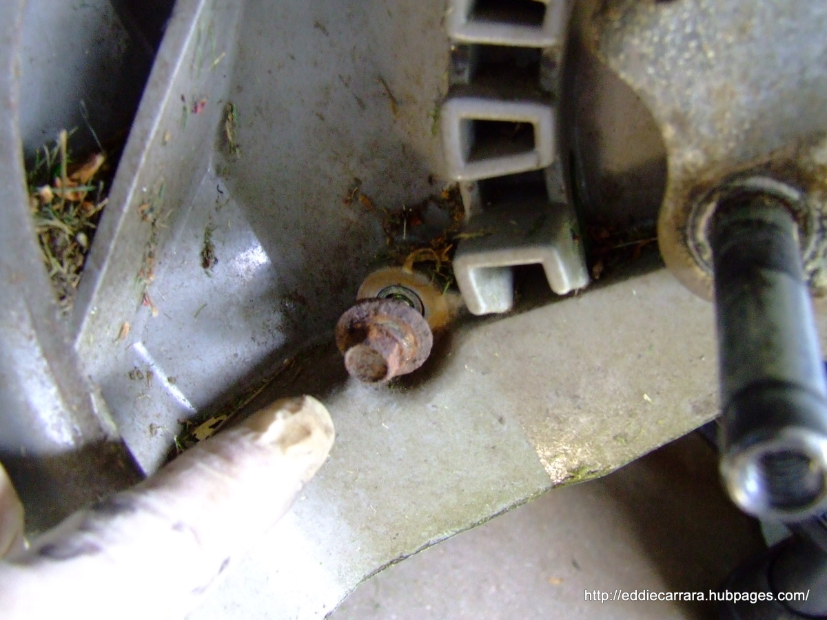 Remove the bolt for the bottom deck cover from behind the left wheel height adjuster on the Honda Harmony 215.