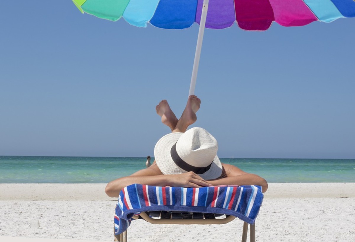 a woman on the beach laying on a chair under an umbrella