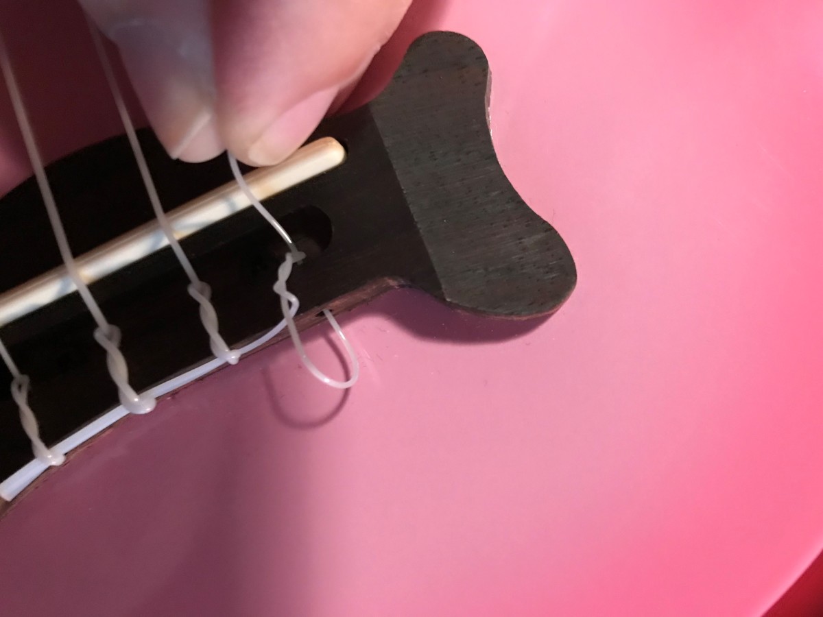 Removing old strings from ukulele with a tie-bar bridge.