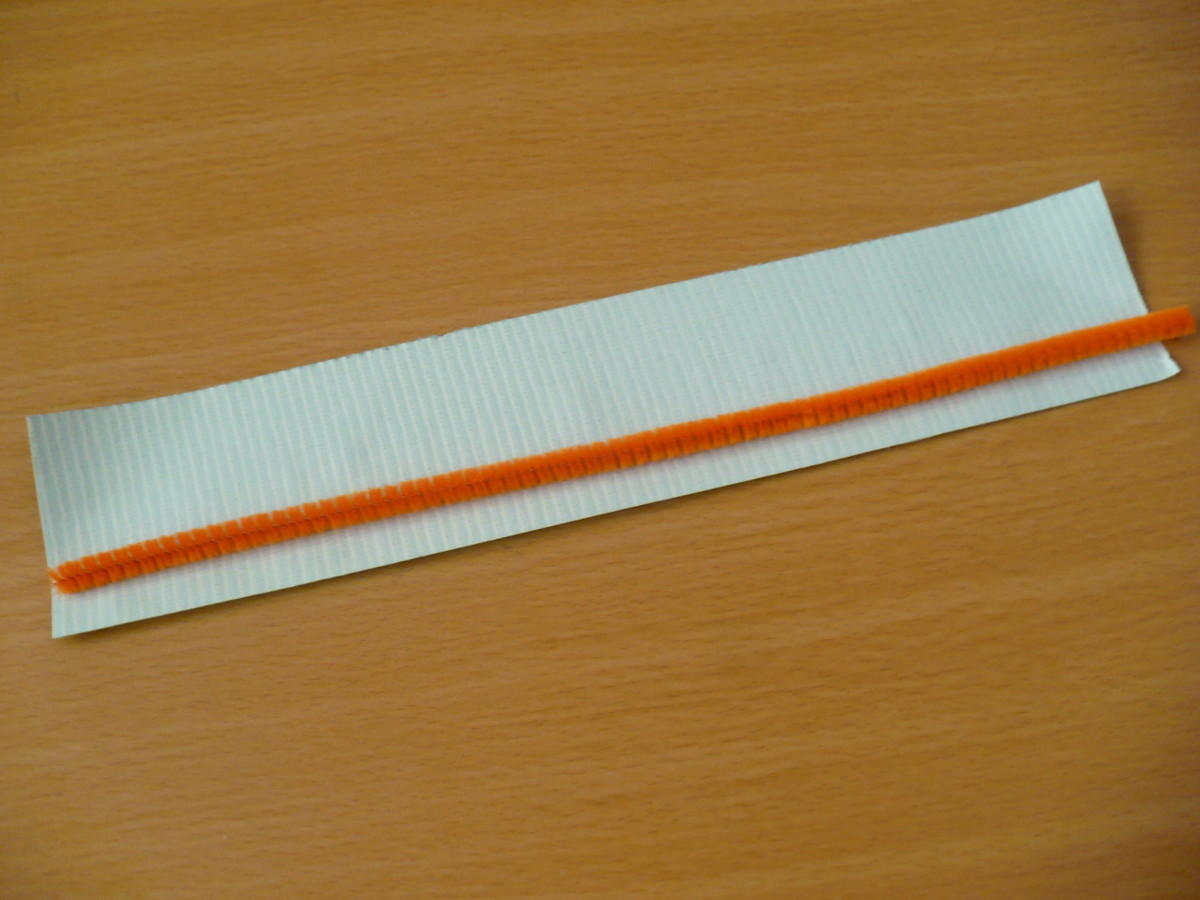 Cut a strip of green duct tape approximately the same length as a pipe cleaner (orange).