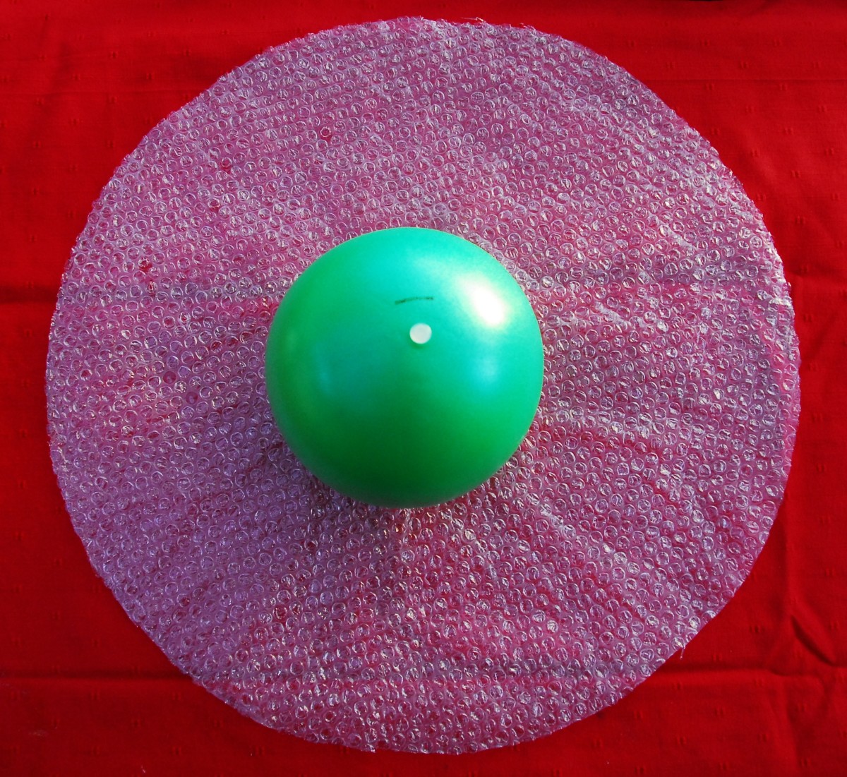 Cut a circle out of bubble wrap.   The diameter  should be sufficient to enable you to wrap the ball up in the bubble wrap with the end open,  just short of the valve or knot in the balloon, Place on a towel or alternatively some bubble wrap,