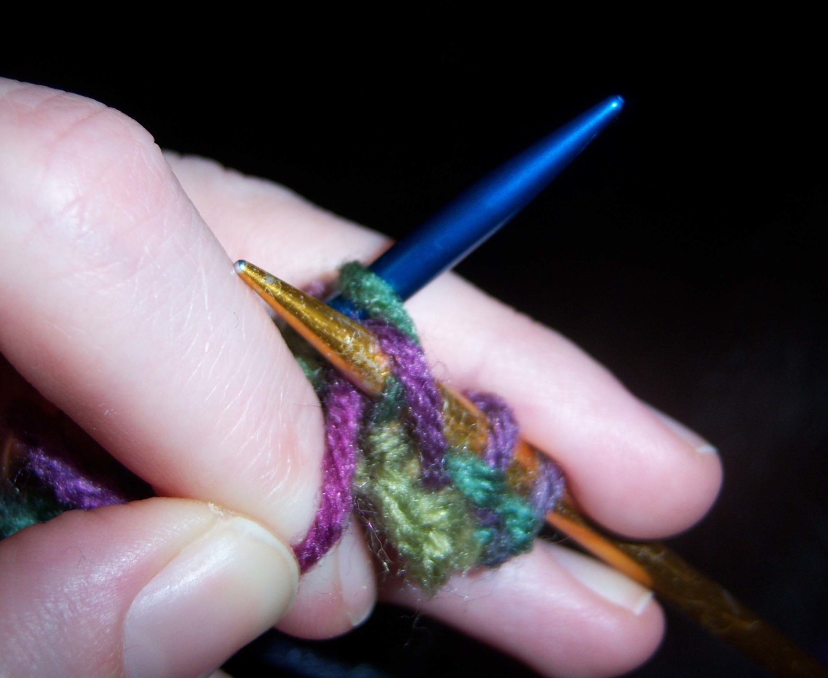 After the gold needle was inserted through the stitch on the blue needle, the yarn is pulled over the tip of the gold needle.