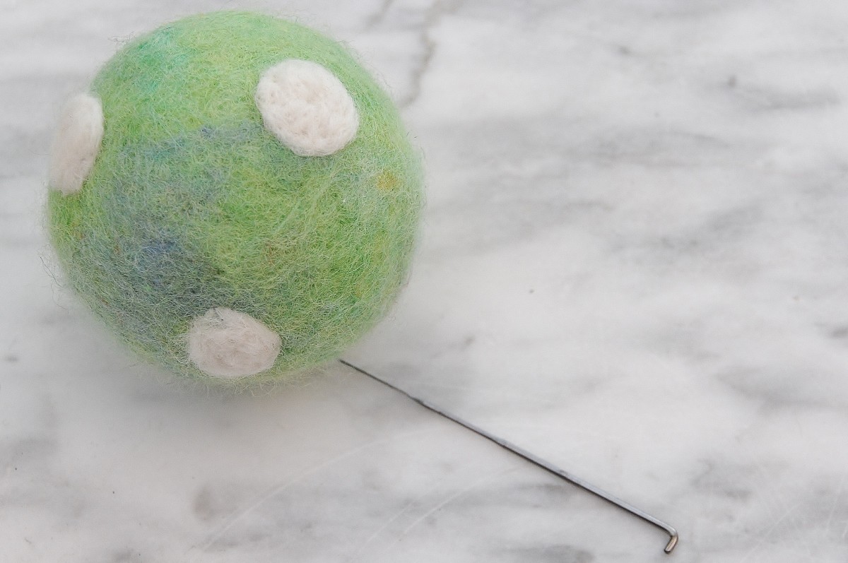 Needle felting white polka dots on the surface of the felted ball