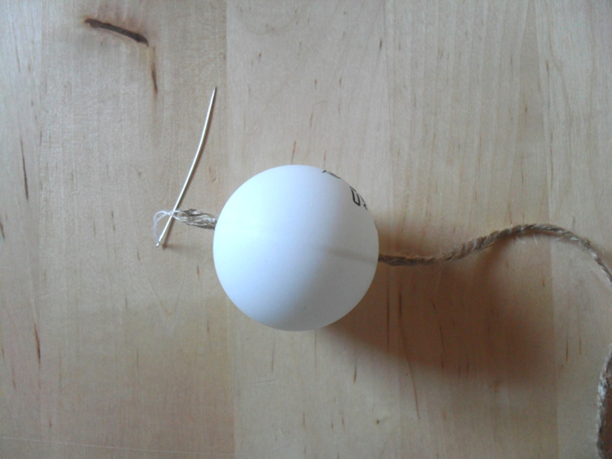 The twine is pulled through the hole in the ping pong ball.