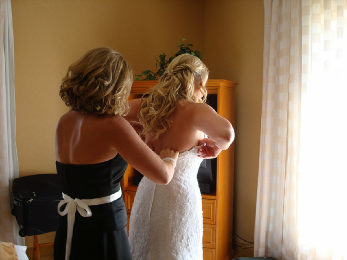 The maid of honor helps the bride in many ways, including getting dressed on the wedding day.