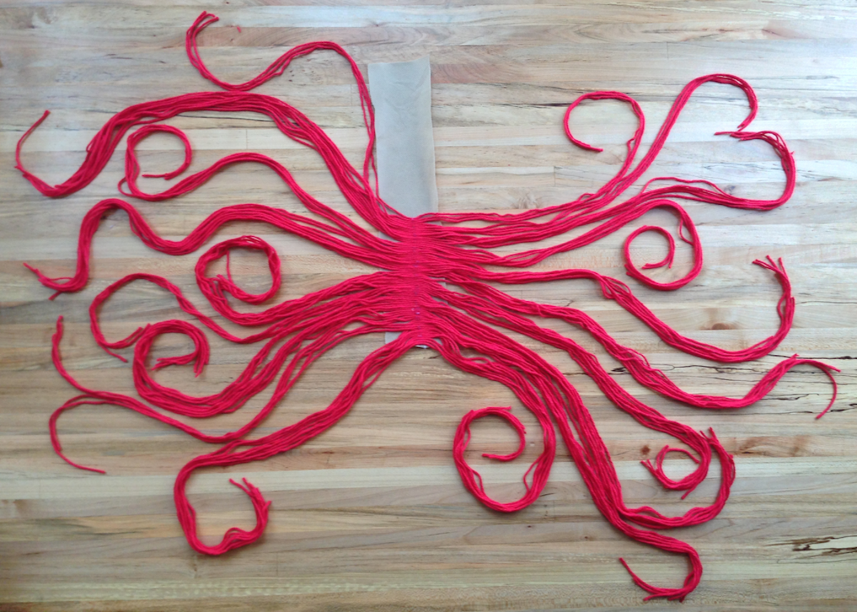 Here, half of the yarn has been attached to the strip of fabric. Continue until you use all of the red strands.