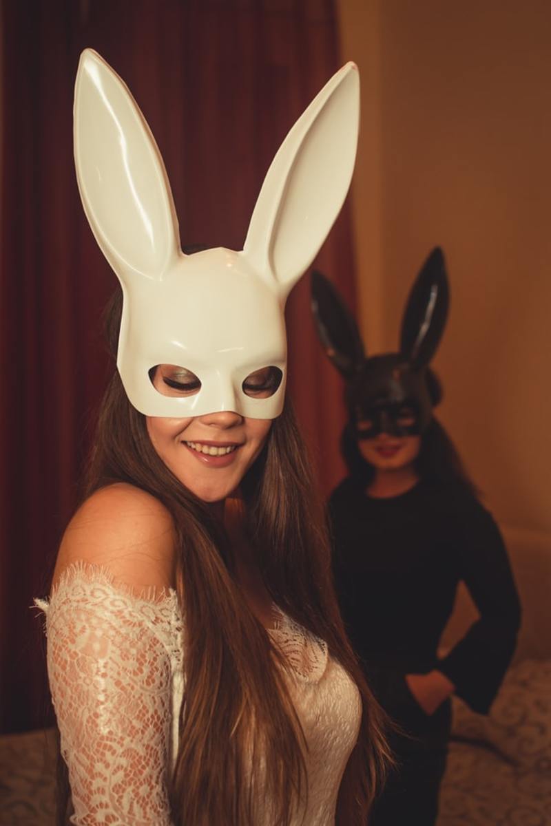 Two woman dressed in fitted garments wearing half face masks with rabbit ears.