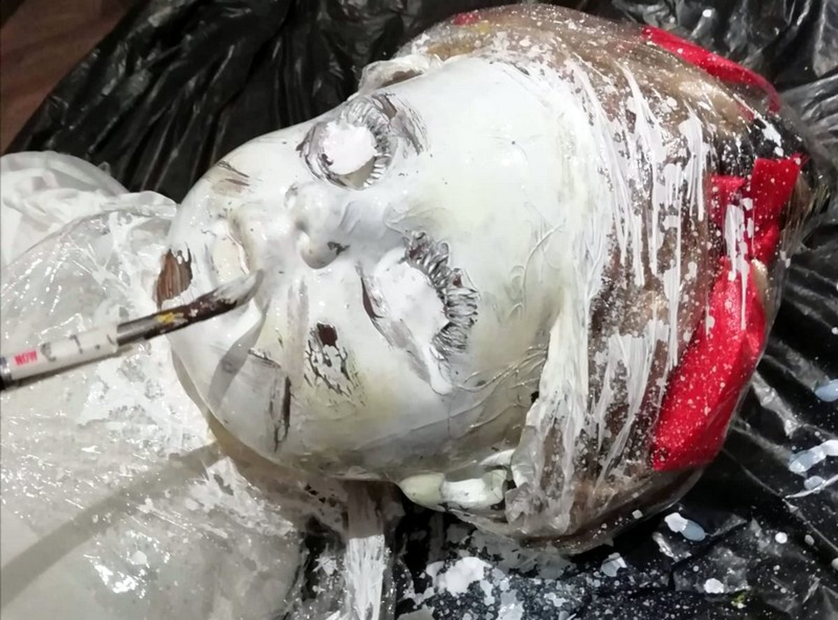 Here I paint the doll's head white after covering its eyes with tape. 