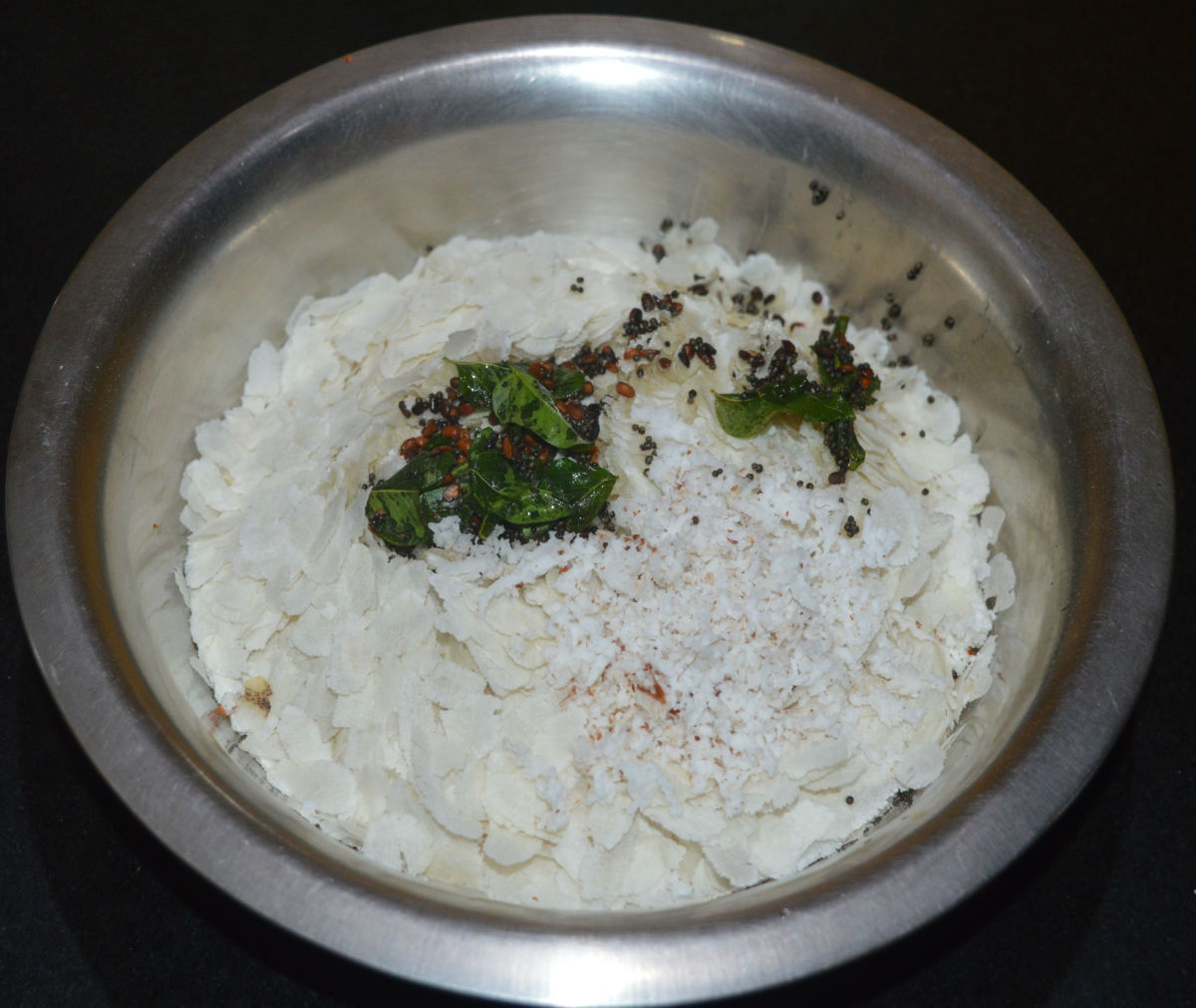 Add the tempering to the bowl containing flattened rice and the masala paste. Add the remaining grated coconut.