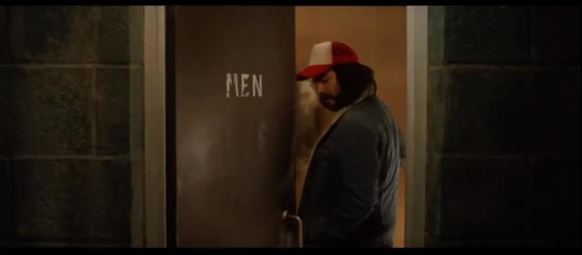 Mid-shot of The Trucker (Adam Lambert) closing the men's room door.