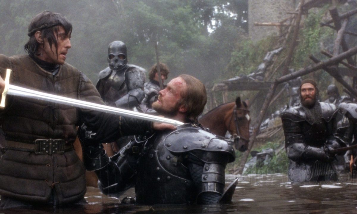 Arthur (Nigel Terry) holds Excalibur to Uryens (Keith Buckley) 