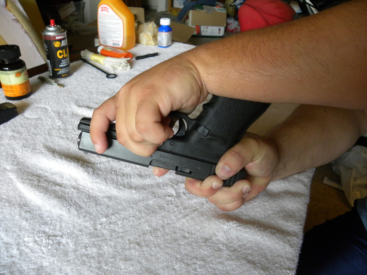 Just above the edge of the trigger guard is a rectangular pin that can be slid upwards, releasing the slide from the frame. With thumb and forefinger, grip the pin, and slide it upwards, holding it in place there.