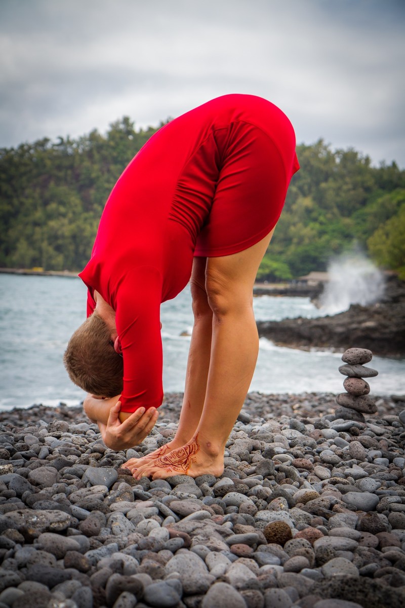 A yogi doing standing forward fold pose outdoors.