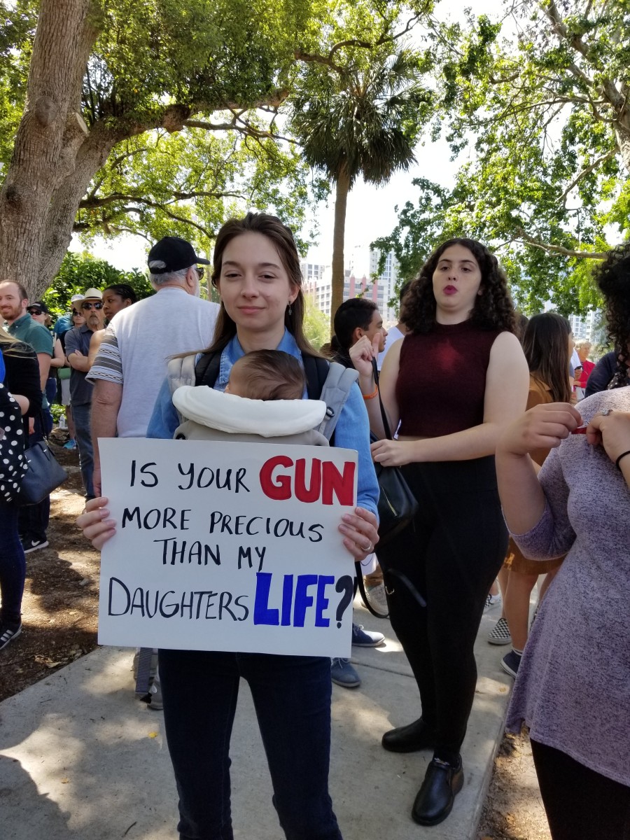 The sign says, "Is your gun more precious than my daughter's life?"