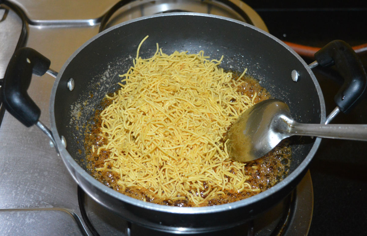 Step four: Add sev. Gently, mix it with the syrup. Keep a steel plate ready for pouring the hot sev chikki liquid.